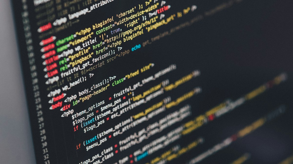 Close-up of a laptop screen showing code in an editor on a developer desk